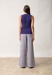 Bezramenný fialový pletený top v kombinaci s širokým pruhovaným kalhotami v světlé fialové a bílé barvě. Obsahuje přiléhavý korzet a jemnou strukturu.