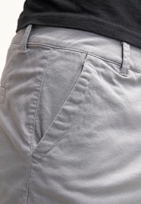 Lichtgrijze katoenen broeken met een gladde textuur, schuine zijzakken en gedetailleerde stiksels langs de naden.