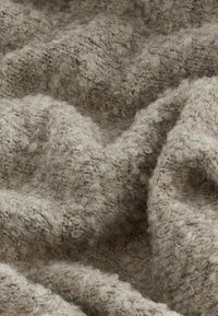 Texturerad tyg med en mjuk, lurvig yta i ljusbeige. Materialet verkar tjockt och mysigt, med ett löst, ojämnt vävmönster.