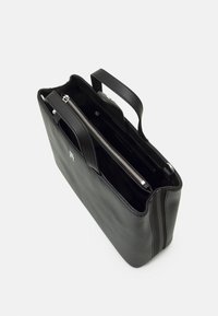 Sac fourre-tout en cuir noir avec une texture lisse, des poignées supérieures et un compartiment zippé. Présente un matériel minimal et un design épuré.