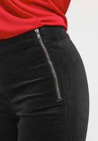 Los pantalones de ante sintético negros presentan un detalle de cremallera lateral, una textura suave, un corte ajustado y un diseño de cintura alta. La tela tiene un suave brillo.