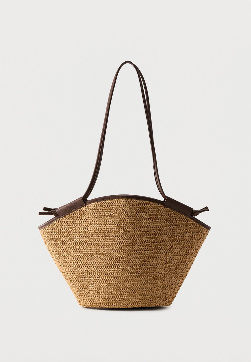 Πλεκτή τσάντα από ψάθα με σκουρόκαφέ δερμάτινη επένδυση και μακριά ρυθμιζόμενα λουριά ώμου, σχήμα τραπεζίου σε λευκό φόντο.