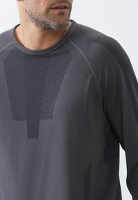 Grijze langemouwen shirt heeft een gestructureerd patroon, soepele stof en raglan mouwen, met subtiele geometrische accenten over de voorkant.