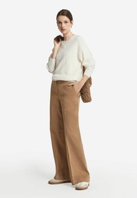 Biała sweter z dzianiny z teksturowanym dekoltem, zestawiony z brązowymi spodniami o szerokich nogawkach z wysokim stanem. Modelka trzyma brązową pikowaną torebkę.