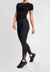 Top atletico nero a maniche corte, abbinato a leggings neri con stampa a chevron grigia. Scarpe da ginnastica nere completano l'outfit.