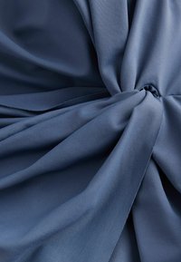 Donkerblauwe stof met een gladde, zachte textuur, gekenmerkt door draaien en plooien die diepte en beweging in het materiaal creëren.
