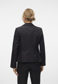 Svart skreddersydd blazer laget av glatt stoff, med en tettsittende silhuett, lange ermer og en enkelt vent bak.