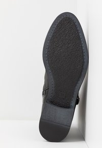 Semelle de bottine noire avec grip texturé, taille 37 marquée près du talon, photographiée en vue inclinée sur fond blanc.