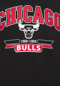 T-shirt nera con testo audace in bianco e rosso "CHICAGO" sopra un logo di un toro con dettagli rossi. Include "1968-1969" e "BULLS" in rosso.