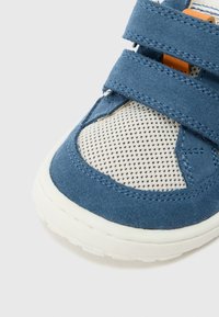 Μπλε μοκασίνι από σουέτ με μπεζ δίχτυ, διαθέτει δύο ιμάντες με βέλκρο και υφή στη σόλα από καουτσούκ, λεπτομερή ραφές και πορτοκαλί πινελιές.