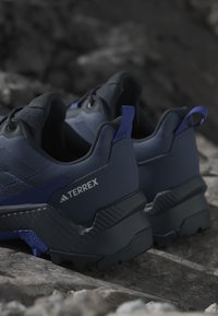 Blå och svarta Terrex vandringsskor med texturerade material, en robust sula och en bakre dragöglan, med diskret varumärkessynlighet.