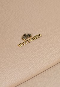 Sac en cuir beige avec une texture granuleuse ; présente un logo doré et des détails accentués. Design lisse et structuré avec des lignes épurées.