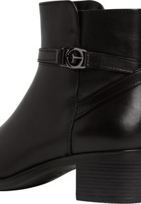 Botín negro de cuero hasta el tobillo con puntera redonda, tacón delgado, correa decorativa con hebilla y detalles de costura. Acabado brillante con suela texturizada.