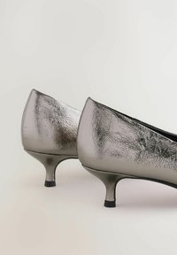 Chaussures à talons hauts en argent métallique avec une finition texturée, présentant un bout pointu et un petit talon, sur un fond clair.
