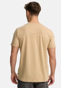 Tan kortærmet t-shirt med et tekstureret øverste panel. Glat stof, afslappet pasform og rund hals. Sideetiket synlig.