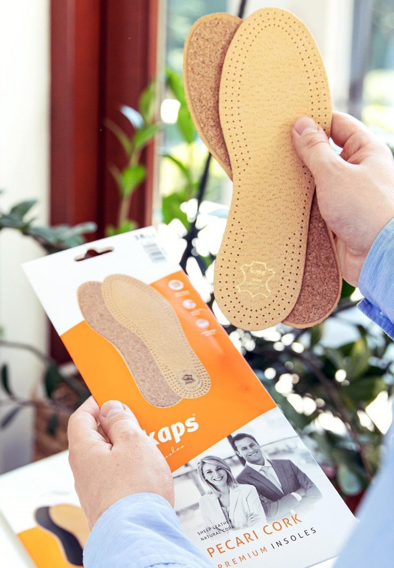 Cork insoles with perforated design, held next to packaging featuring sheep leather and natural cork. Colors: light brown and orange.