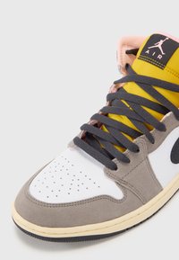 Gray and white sneaker with a partially yellow upper, black accents, gray laces, and perforated toe. Rubber outsole with textured design.