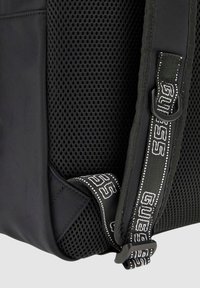 Zaino nero con una combinazione di tessuto morbido e sezioni in rete. Cintura regolabile con dettagli del marchio e attacco a gancio.