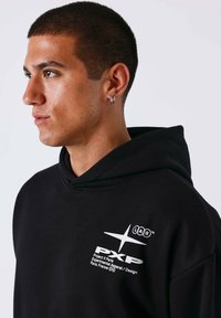 Zwarte hoodie met een voorzak, voorzien van een witte grafische print en logo op de borst, gemaakt van zachte stof met een relaxte pasvorm.