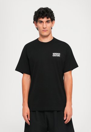 Svart bomull T-skjorte med rund hals og korte ermer, med en hvit "VERSACE COUTURE" logo på venstre brystområde.