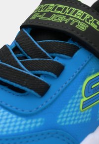 Modré tenisky Skechers S-Lights s černými tkaničkami a neonově zeleným logem na jazyku a boku, detailní záběr na horní přední část.