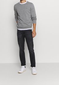 Grauer Baumwollpullover mit Rundhalsausschnitt, kombiniert mit dunklen Jeans und weißen Sneakers. Auffällige Merkmale sind der gerippte Saum und die Ärmel.