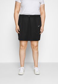 Černá sportovní sukně s elastickým pasem a stáhnutím, s postranními kapsami a logem Nike. Hladká textura a délka ke kolenům.