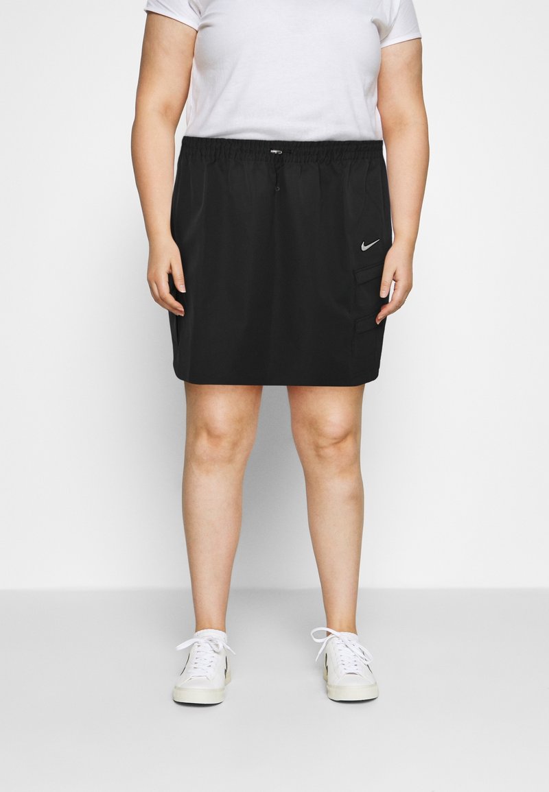 Černá sportovní sukně s elastickým pasem a stáhnutím, s postranními kapsami a logem Nike. Hladká textura a délka ke kolenům.