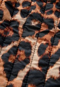Gros plan d'un tissu matelassé avec un motif léopard marron, beige et noir et des lignes de couture verticales.