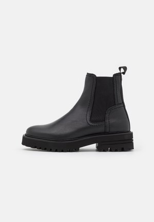Schwarzer Chelsea-Stiefel aus Leder mit elastischen Seitenteilen, Zuglasche hinten, grob profillierter Sohle und niedrigem Absatz.