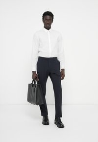 Bela srajca z gumbi v kombinaciji s temno mornarskimi krojenimi hlačami. Črna usnjena torba, držana z eno roko, polirane črne čevlje, preprost in sodoben dizajn.