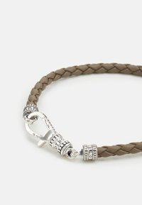 Bracciale in pelle intrecciata marrone con hardware in tonalità argento, dettagli incisi e chiusura a gancio. Texture liscia con un design minimalista.