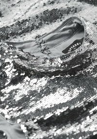 Stříbrná flitrová tkanina s hladkým šedým podšívkou. Má zahnutý výstřih a štítek s názvem značky "Superdry". Lesklá, odrážející textura.