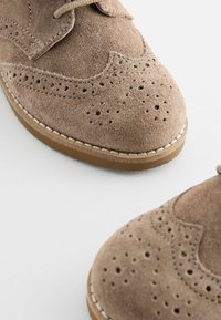 Chaussures habillées en daim marron avec un design à bout relevé, des détails perforés et une semelle en caoutchouc marron clair avec un bord cousu.