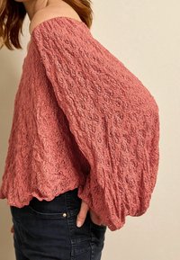 Skulderfri, struktureret bluse i støvet rosa med blomsterprint, der har bløde ærmer og en bølget kant. Sættes sammen med mørke jeans.