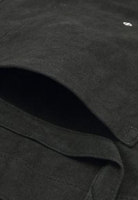 Black canvas tote with a simple design, featuring stitching details and an open pocket. The texture appears smooth and durable.