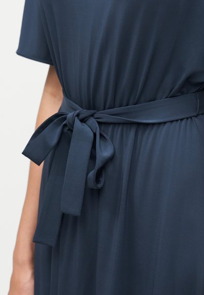 Gros plan d'une robe bleu foncé avec une ceinture en tissu nouée autour de la taille et des manches courtes, portée par une personne.