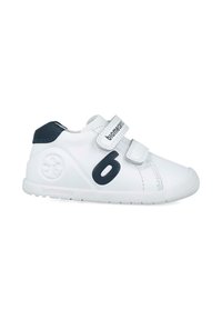 Zapatos blancos para niños con acentos en azul marino, tiras de Velcro, punta redondeada y un logo circular. Suela texturizada para agarre y flexibilidad.