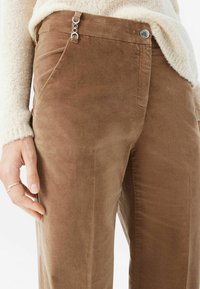 Bruna kordflamsbyxor med en mjuk textur, har en sidoficka och silverdetaljer vid midjan, och har en avslappnad passform.