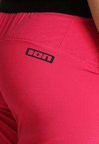 Pink athletic pants made from stretchy fabric, featuring a black ION logo near the waistline and subtle textured detail on the lower edge.