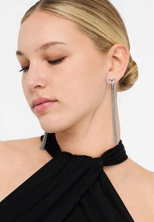 Sølv øreringe med dusk og dobbelte cirkulære accenter, prydet med rhinsten, hængende fra en cylindrisk stift. Sort beklædningsbaggrund.