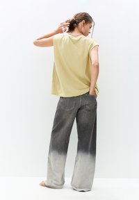 Lys gul oversized t-shirt med korte ærmer, parret med grå ombré brede jeans med baglomme og frynsede sømme.