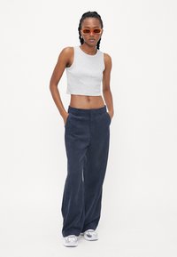 Grå kort tanktopp, marineblå vide bukser, sølvfargede joggesko og oransje solbriller. Glatt stoff med en avslappet passform og enkel design.