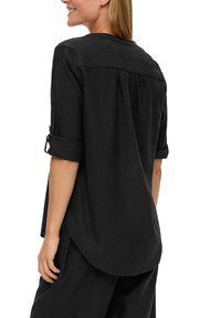 Chemise en lin noire avec un ourlet arrondi, des manches retroussables et un empiècement au dos avec des plis pour une texture supplémentaire.