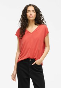 Top coral de cuello en V en tejido suave, con mangas cortas y corte relajado, combinado con pantalones negros de cintura alta. Diseño liso sin patrones visibles.