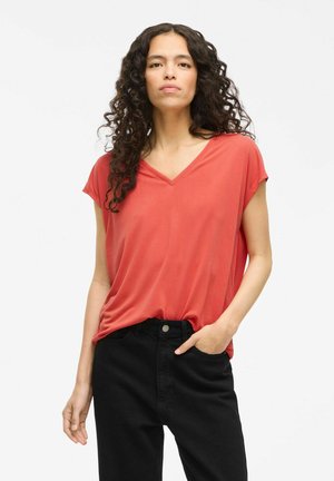 Top coral de cuello en V en tejido suave, con mangas cortas y corte relajado, combinado con pantalones negros de cintura alta. Diseño liso sin patrones visibles.
