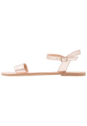 Metallic rose gold sandals with a flat sole, open toe, and ankle strap featuring a buckle detail. Slim, minimalist design.