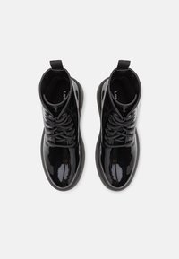Botines de charol negro hasta el tobillo, con punta redonda, cordones en la parte frontal y tira en la parte trasera. Textura suave y suela gruesa.