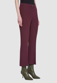 Pantaloni su misura color marrone scuro con vestibilità aderente, caratterizzati da un dettaglio a fibbia dorata in vita. Abbinati a stivaletti a punta verde oliva.