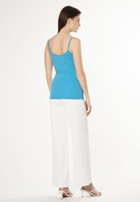 Turquoise getaillede tanktop met dunne bandjes, gecombineerd met witte wijde broek en witte hakken. Soepele, rekbare stof.